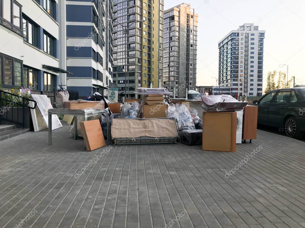 Many different things of furniture stand unloaded on the street near the house of the skyscraper new building. Concept: relocation, housewarming