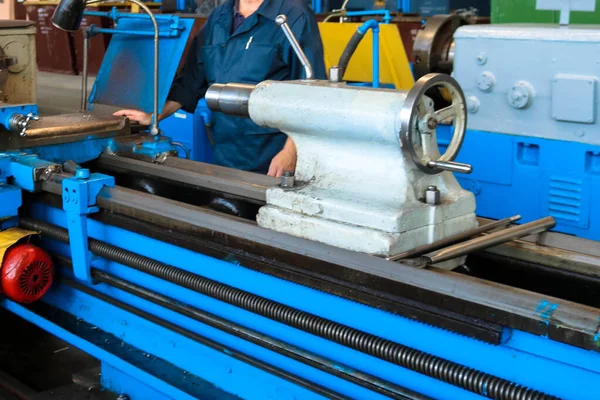 Grote metalen ijzeren industriële draaien en schroef snijmachine voor de verwerking van metaal en onderdelen met reserveonderdelen en een werknemer in een badjas in de fabriek — Stockfoto