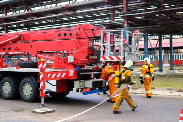 Firemen rescue workers in fireproof suits came to extinguish a fire in a fire truck and stretch the hoses in a large industrial plant with pipes and equipment