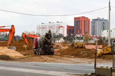 Traktör kazıcıları ve buldozerlerden oluşan çok sayıda güçlü endüstriyel uzmanlaşmış inşaat ekipmanı büyük bir şehirde yeni bir mikro bölge inşaatı sırasında yol onarımı yapıyor.