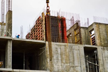Çalışan erkek inşaatçılar büyük bir monolitik çerçeve, bina ve inşaat halindeki yeni bir binanın çatısında çalışıyorlar. Binanın inşaatı büyük şehrin yeni mikro bölgesinde.