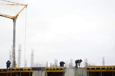 Çalışan erkek inşaatçılar büyük bir monolitik çerçeve, bina ve inşaat halindeki yeni bir binanın çatısında çalışıyorlar. Binanın inşaatı büyük şehrin yeni mikro bölgesinde.
