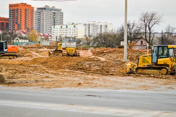 Many powerful industrial heavy specialized construction equipment of tractor excavators and bulldozers make road repairs during the construction of a new micro-district in a big city