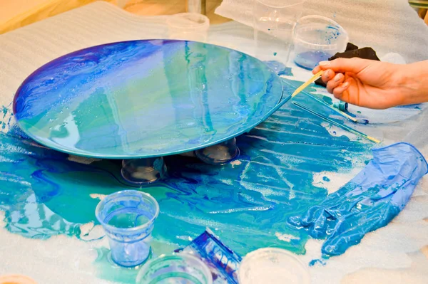 Процесс создания самодельной модной абстрактной современной картины, окрашенной кистью из акриловой синей разноцветной смолы на круглой деревянной доске — стоковое фото