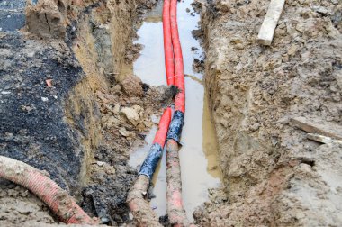 Yeni bir yeraltı topluluğunun onarımı sırasında bir inşaat alanındaki trafo alt istasyonunun kablolarına bağlı büyük kırmızı plastik borular.