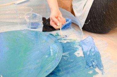 Yuvarlak ahşap bir tahta üzerinde akrilik mavi çok renkli bir reçine fırçasıyla boyanmış ev yapımı soyut bir modern model yaratma süreci.