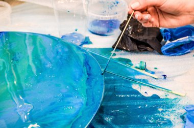 Yuvarlak ahşap bir tahta üzerinde akrilik mavi çok renkli bir reçine fırçasıyla boyanmış ev yapımı soyut bir modern model yaratma süreci.