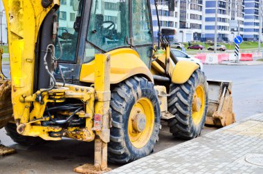 Büyük, sarı, güçlü endüstriyel kazıcı traktör, buldozer, büyük bir şehirde yeni bir mikro bölge inşaatı sırasında yol onarımı için özel inşaat ekipmanları.
