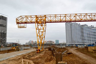 Çağdaş bir inşaat şantiyesinde kargo taşımak için desteklere bağlı durağan, ağır, sarı, demir ağırlıklı, sanayi tipi, güçlü, köprü tipi vinç.