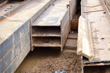 Açık hava şantiye deposunda metal parçaları, çubukları, kirişleri ve boruları olan bir sürü inşaat malzemesi var.