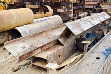 Açık hava şantiye deposunda metal parçaları, çubukları, kirişleri ve boruları olan bir sürü inşaat malzemesi var.