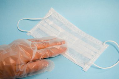 Plastik eldivendeki bir el, mavi arka planda Coronavirus covidum-19 'un ölümcül mikrop ve virüs hastalıklarına karşı korunmak için tek kullanımlık koruyucu bir maske bulundurur.