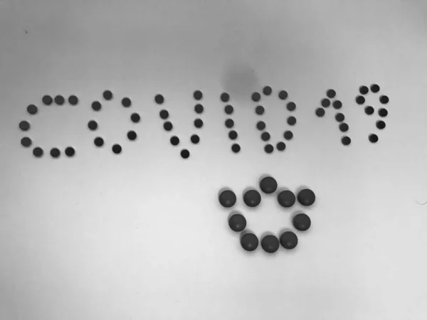 Черно-белая надпись Ковид-19 выполнена из круглых желтых лекарственных таблеток коронавируса для лечения пандемических заболеваний и вирусов. Фон — стоковое фото