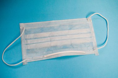 Mavi arka planda Coronavirus covid-19 virüslü tehlikeli mikrop ve virüslere karşı korunmak için tek kullanımlık beyaz tıbbi maske.