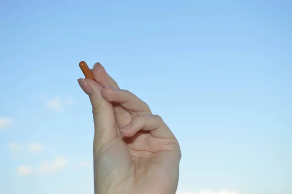 Beautiful female hand holds a medical pharmaceutical pill capsule from coronavirus covid-19 for the treatment of diseases and viruses on a blue sky background