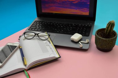 Evde iş yeri, bilgisayarlı cep telefonu akıllı cep telefonu kalem kulaklık ve pembe ve mavi arka planda gözlük ile uzaktan çalışma merkezi.