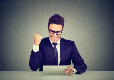 Excited business man reading good news on line on a tablet computer clipart