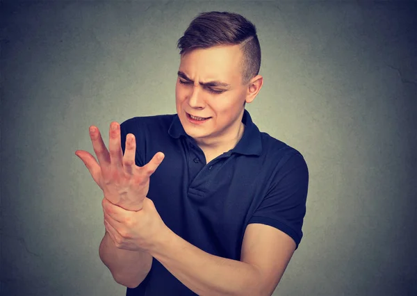 Junger Mann, der sein schmerzhaftes Handgelenk isoliert auf grauem Wandhintergrund hält. Verstauchungsschmerzen — Stockfoto