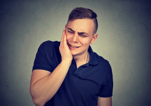 Zahnschmerzen. frustrierter junger Mann in Schmerzen, die seine Wange berühren — Stockfoto