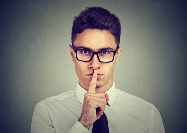Keep my secret. Businessman holding finger on lips looking at camera 
