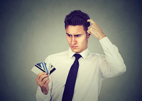 Hombre confundido mirando muchas tarjetas de crédito incierta cuál elegir —  Fotos de Stock