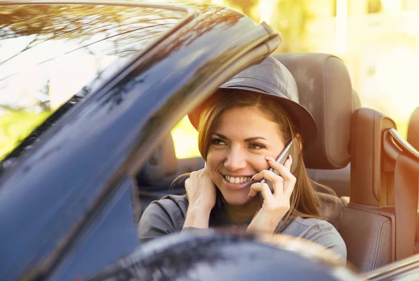 Mujer feliz sentada en un coche nuevo convertible hablando por teléfono móvil en un día soleado —  Fotos de Stock