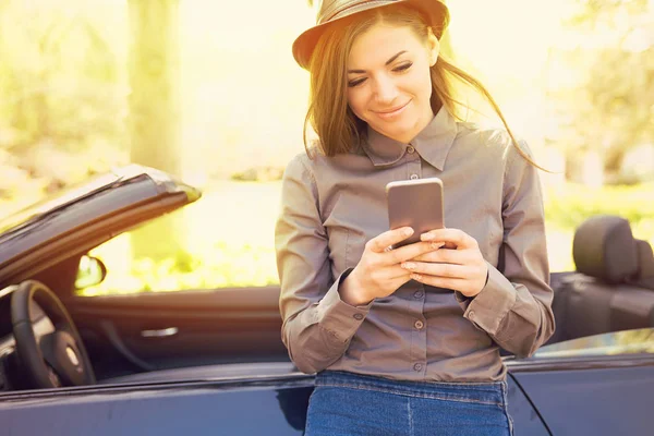 Mujer exitosa de pie junto a su coche mensajes de texto en el teléfono móvil —  Fotos de Stock