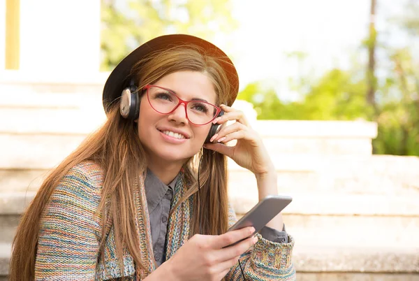 Bella ragazza adolescente che ascolta la musica su uno smartphone seduto sulle scale nel parco urbano — Foto Stock