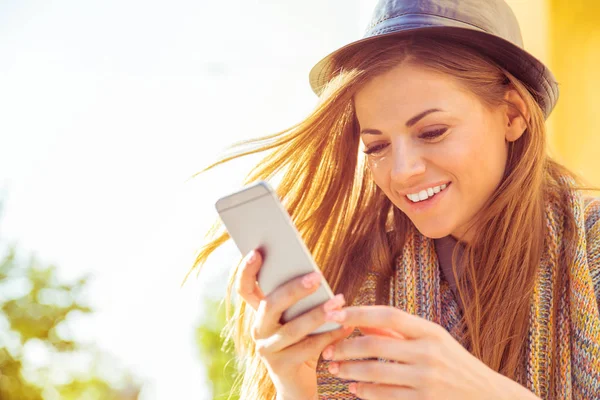 Szczęśliwa kobieta siedzi na zewnątrz SMS-y na inteligentny telefon na ulicy na jesień, słoneczny dzień — Zdjęcie stockowe