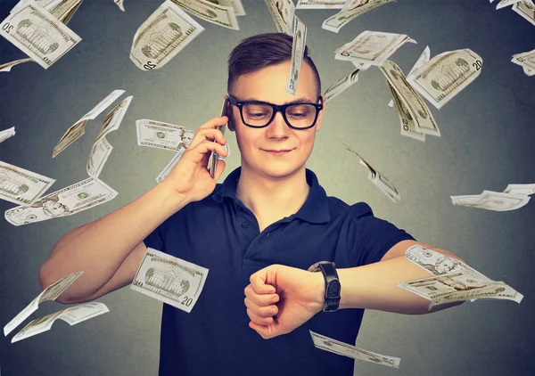Geschäftiger Geschäftsmann, der auf die Armbanduhr schaut, im Geldregen mit dem Handy telefoniert. Zeit ist Geld — Stockfoto