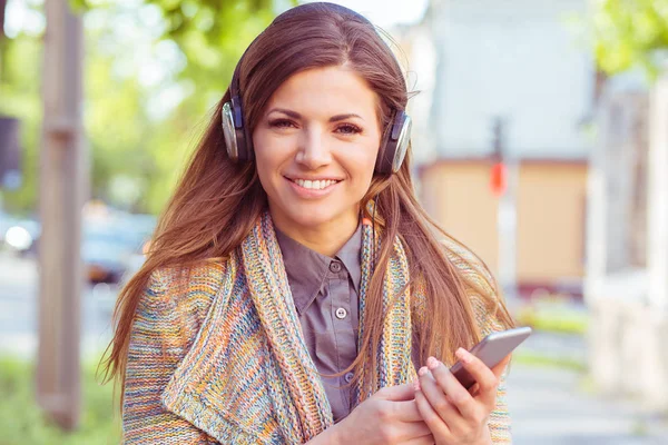 Chica feliz escuchando música con auriculares en un teléfono inteligente en la calle en un día soleado de otoño — Foto de Stock