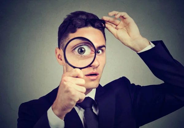 Curious young man taking off glasses looking through a magnifying glass — Stock Photo, Image