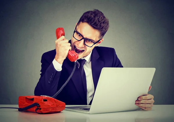 Злой молодой бизнесмен звонит в службу поддержки клиентов с отказом ноутбука, крича по телефону — стоковое фото