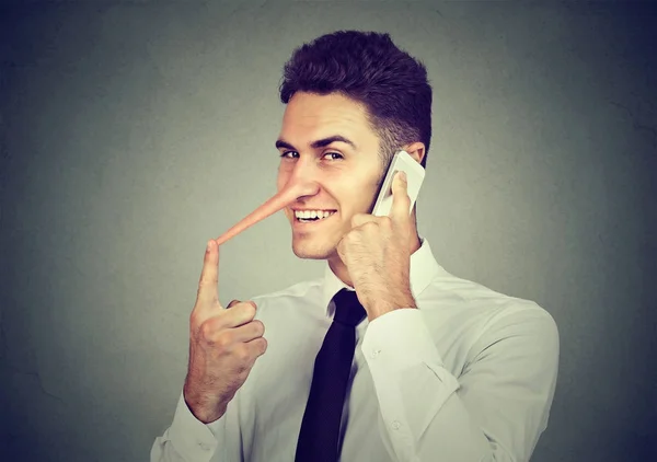 Schlitzohriger junger Mann mit langer Nase, der isoliert auf grauem Wandhintergrund mit dem Handy spricht. Lügenkonzept. — Stockfoto