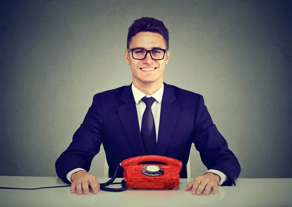 Homem de negócios feliz sentado na mesa com telefone vintage olhando para a câmera — Fotografia de Stock