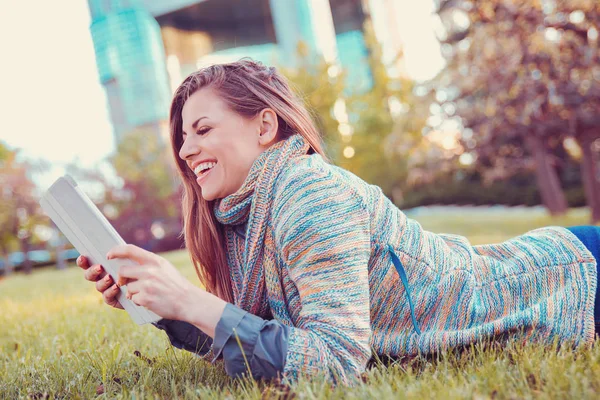 Mujer joven usando tableta al aire libre acostado en la hierba en un parque de la ciudad — Foto de Stock