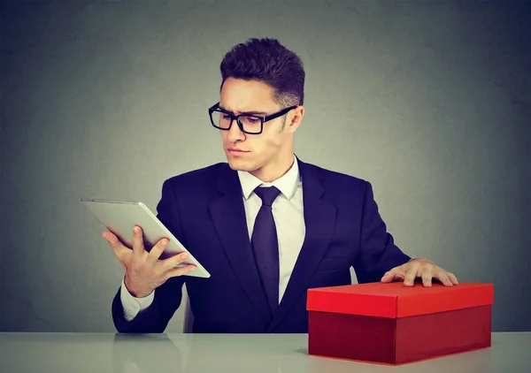 Hombre con caja de regalo de compras revisando el nuevo producto en línea en su tableta —  Fotos de Stock