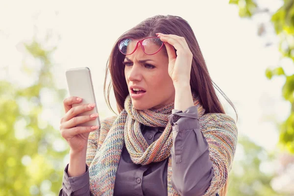 Rahatsız kadın gözlük bir sonbahar gününde bir sokakta yürürken hayal kırıklığı ile akıllı telefonunu arıyorum  