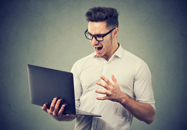 Angry młody człowiek oglądając laptopa w rage — Zdjęcie stockowe