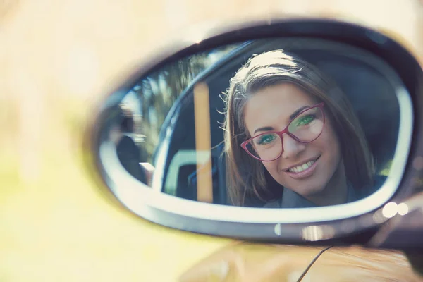 Woman driver looking in the side view mirror of her new car — Stock Photo, Image