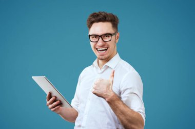 Heyecanlı genç adam beyaz gömlek ve gözlük jest Yaşasın vererek tablet PC'yi kullanma