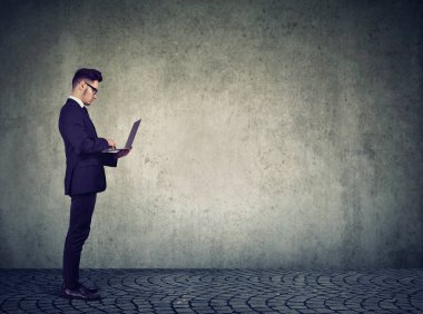 Dizüstü tutarak ve gri arka plan karşı dururken yazarak kendine güvenen adam 