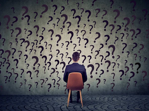 Üzleti ember ül egy széken, egy fal előtt már sok kérdést, vajon mit csináljak — Stock Fotó