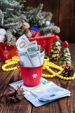 Bükülmüş faturaları kırmızı Noel kova, euro ve pembe macaroons dolar. Yeni yıl hediye