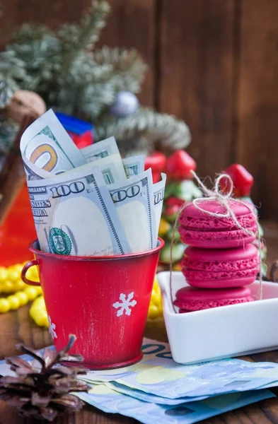 Скрученные долларовые купюры в красном рождественском ведре, евро и розовых макаронах. Новогодние подарки — стоковое фото