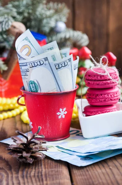 Скрученные долларовые купюры в красном рождественском ведре, евро и розовых макаронах. Новогодние подарки — стоковое фото