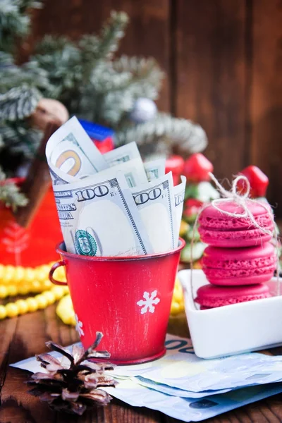 Скрученные долларовые купюры и евро в красном рождественском ведре, евро и розовых макаронах. Новогодние подарки — стоковое фото