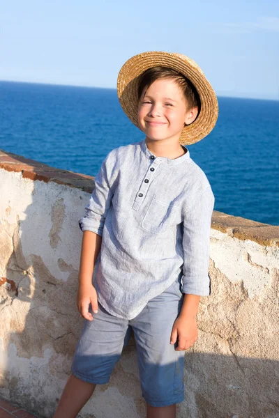 Niño en sombrero de paja sonríe contra el mar — Foto de Stock