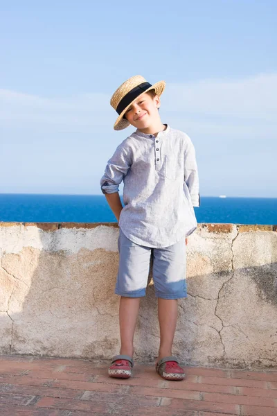 Menino de chapéu de palha sorri contra o mar — Fotografia de Stock