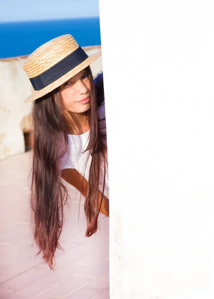 Girl in straw hat peeks out from behind wall — Stock Photo, Image